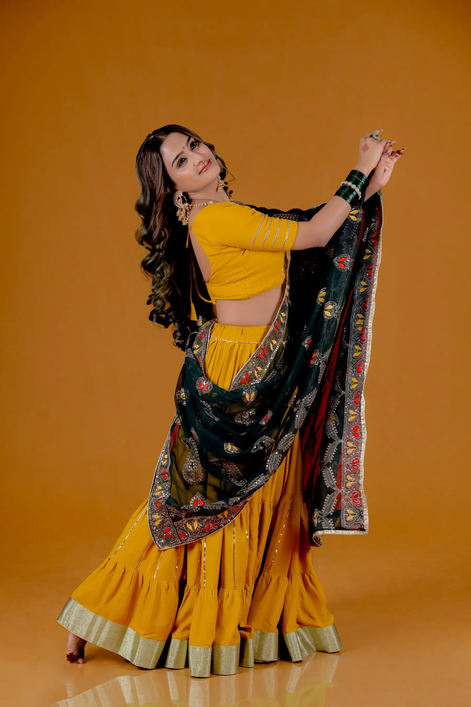 Model in the haldi lehenga swinging a printed dupatta against a mustard wall