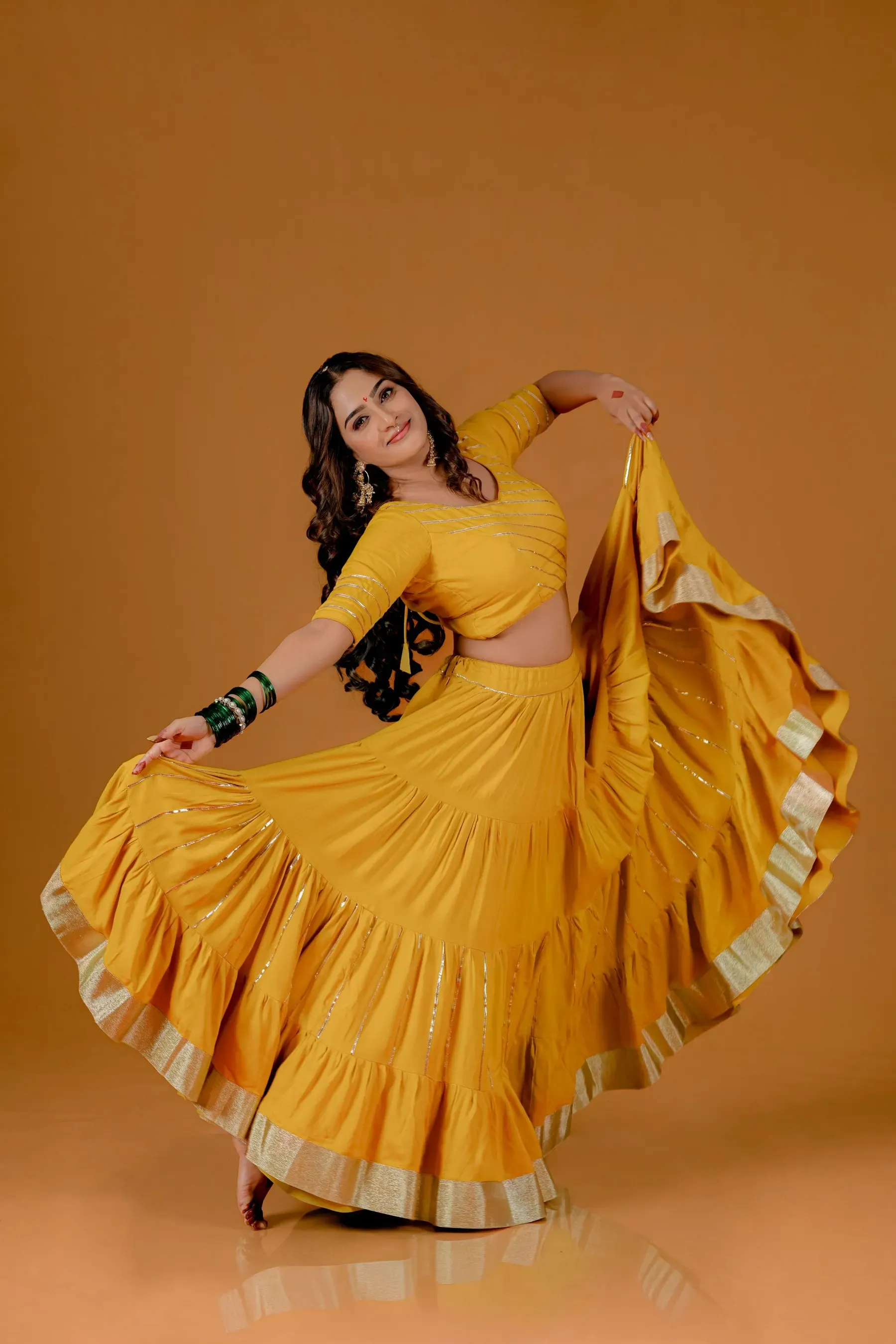 Model holding out a yellow tiered skirt striped with gota lace