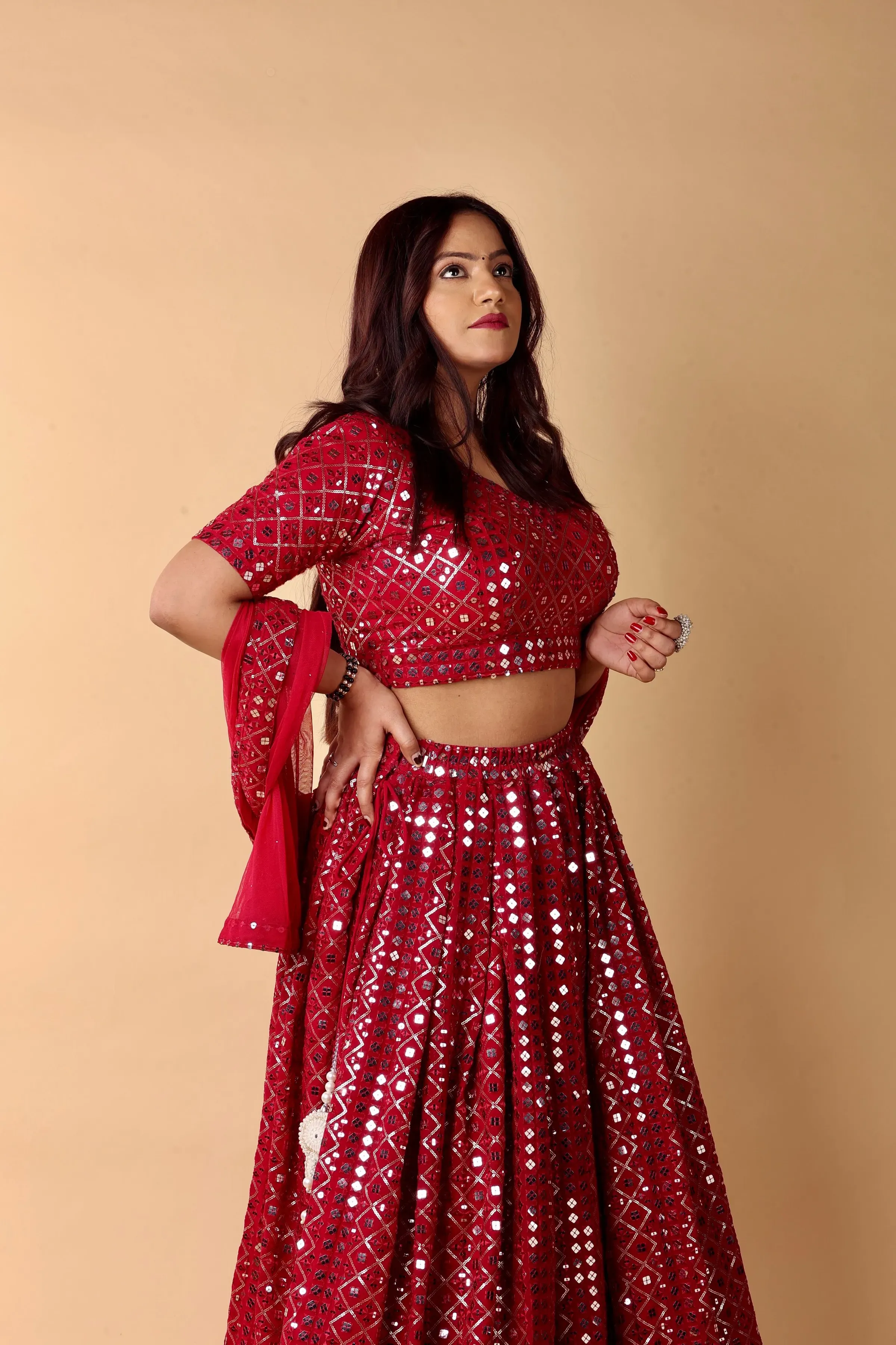 Model in the Anar mirror work lehenga set in red, against a warm beige wall